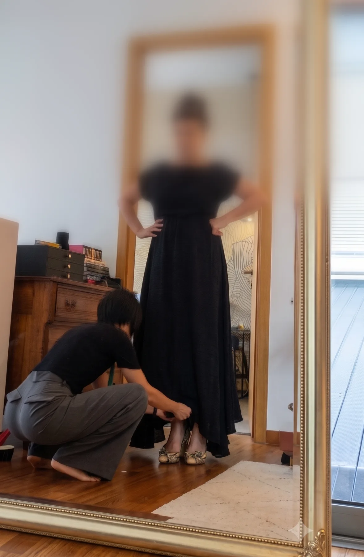 A client in a long black dress watching in the mirror as Hui Ling pins the hem